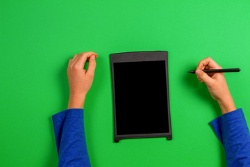 Kid hand with graphic tablet and stylus pen on green background
