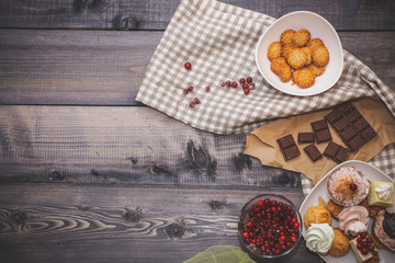 Sesame biscuits in white bowl, dark chocolate broken on craft paper, linen napkin with cranberries on a dark black background of a wooden tabletop