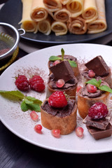 Rolled crepes with chocolate paste topped with raspberries, pomegranate, mint and chocolate pieces on a white plate