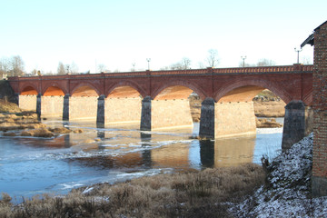 Beautiful red brick bridge view over a small river flowing through village , countryside city.