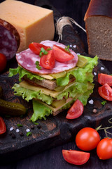 Multi layered club sandwich with rye bread, lettuce salad, sausage, cheese, salted cucumbers and...