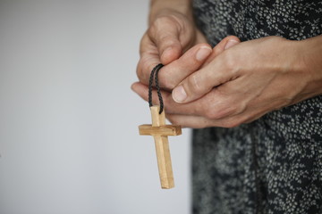 Detailaufnahme von zum Gebet gefalteter Hände mit einem kleinen Kreuz aus Holz