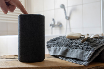 Wooden table with spa towel and voice controlled smart speaker on blurred bathroom shelf background
