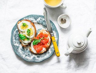 Delicious healthy breakfast or snack - sandwiches with cream cheese, boiled egg and smoked salmon on a light background, top view