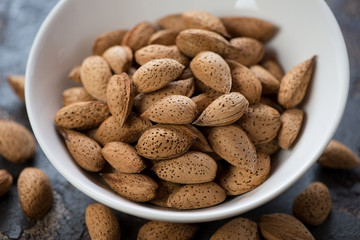 Unpeeled almonds in a white bowl, horizontal shot, closeup