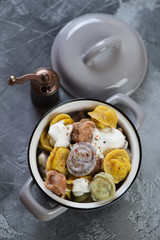 Boiled colored dumplings pelmeni in a pot over grey concrete background, vertical shot, top view