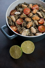 Hemp flour pasta served with mussels and cherry tomatoes, vertical shot on a dark brown metal surface