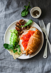 Croissant with cream cheese and smoked salmon, avocado and cherry tomatoes delicious - balanced breakfast, brunch or snack on a grey background, top view