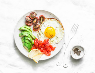 Delicious brunch - fried egg, avocado, cherry tomatoes and smoked salmon on light background, top view