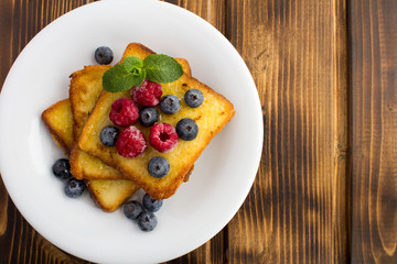 French toasts with berries and honey  in the white  plate on the brown  wooden background.Top...