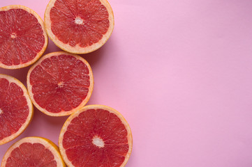 Ripe juicy cut coral color grapefruits on pink background with copyspace.