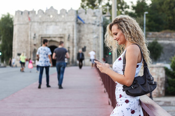 Blonde Girl in a White Dress Standing on the Bridge and Using a Cellphone