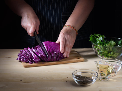 Chef cutting Red Cabbage on wooden table, hands, close up.