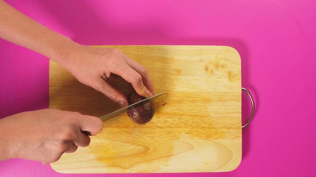 top view, female hand cuts fruit with a knife on a wooden board, maracuya. The concept of natural healthy food.