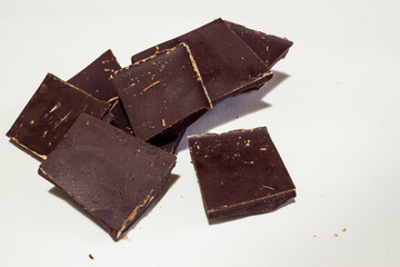 Dark chocolate pieces on white background with fingerprints on it.