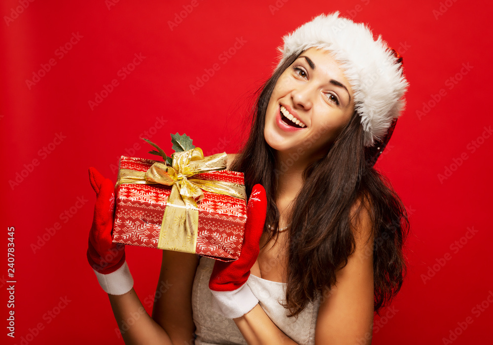 Wall mural beautiful smiling young woman in christmas hat with a gift in hand, close-up