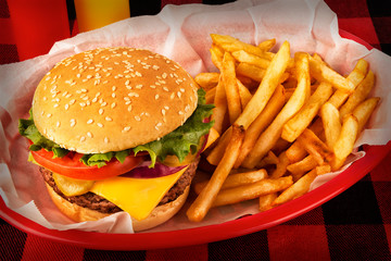 Burger and french fries in basket on tartan tablecloth. Ketchup and mustard bottle in background. Close up. - 240784400