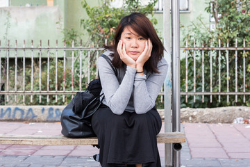 Fototapeta premium Chinese Girl Sitting on the Bench and Thinking While Waiting For Someone
