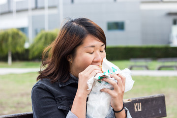 Chinese Girl Sitting on the Bench and Eating Hamburger