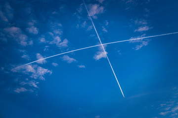 Zwei sich kreuzende Kondensstreifen an azurblauem Himmel mit weißen Wolken
