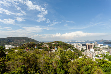 Obraz premium Panoramic view of the city centre of Rio de Janeiro seen trough greenery from a high vantage point with the city and port in the foreground on a bright day with blue sky