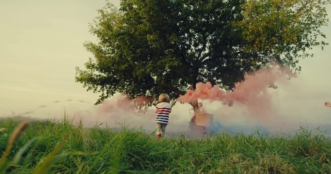 Cute happy little boys in costumes playing with colorful smoke on the hill at the tree. Outdoor.