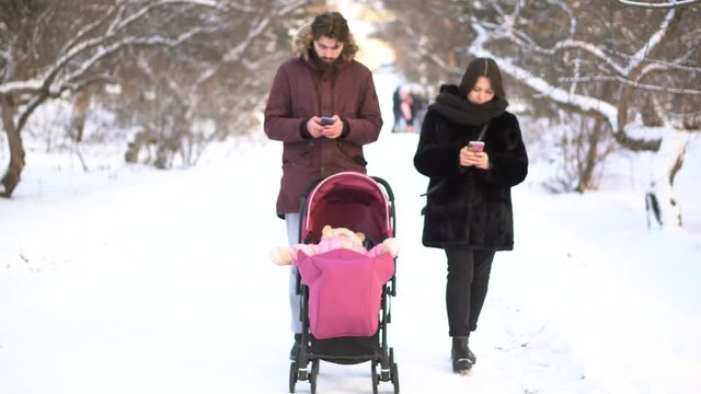 Mother and father addicted to mobile phones neglecting baby in stroller and while walking in winter park. Parents busy with smart phones ignoring little child in stroller, addiction, values concept.