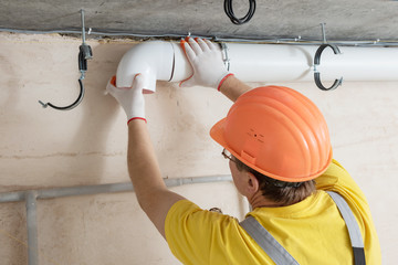 The worker is installing a ventilation system.
