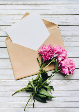Fototapeta Faded purple peonies and an open kraft envelope containing a white sheet of paper. Valentine's Day concept. Copy space, top view.
