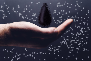 Human hand holding black naphta oil drop. Mixed media.