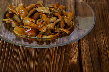 Marinated mushrooms in a transparent plate on a wooden table. Fragment of the dish