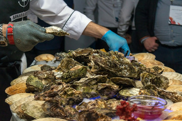A man cleans oysters in shells with iron gloves.