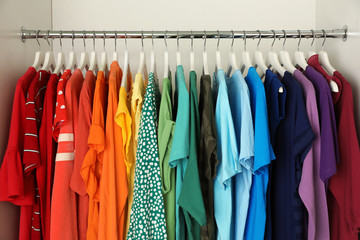 Hangers with different colorful clothes on rack in wardrobe