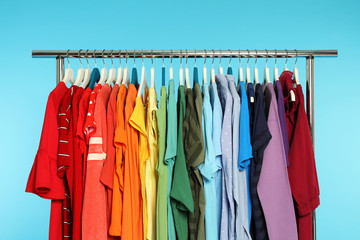 Wardrobe rack with different bright clothes on color background