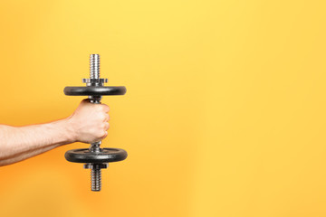 Male athlete holding metal dumbbell on color background. Space for text