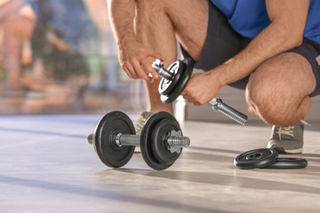 Male athlete with adjustable dumbbells indoors. Space for text