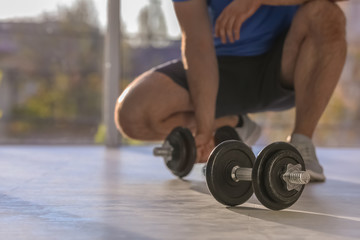 Male athlete with adjustable dumbbells indoors. Space for text