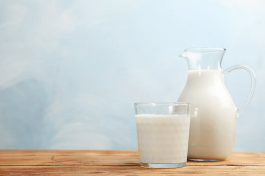 Glass and jug of fresh milk on wooden table against color background. Space for text