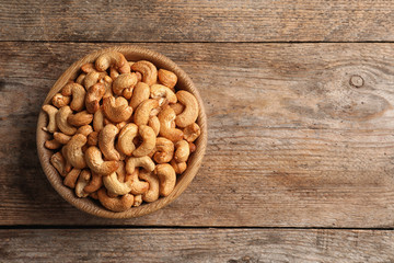 Tasty cashew nuts in bowl on wooden table, top view. Space for text