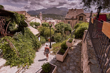 Tourist girl walking on a sunny day in historic downtown of Corte city in Corsica surrounded by mountains