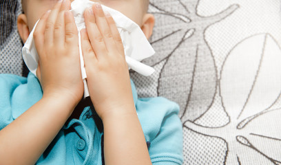 Obraz premium A view of a boy wiping his nose with a hygienic tissue. Medical and health concept, colds. Sick child. Treatment of the child during flu, colds. Cleaning the stuffed nose.