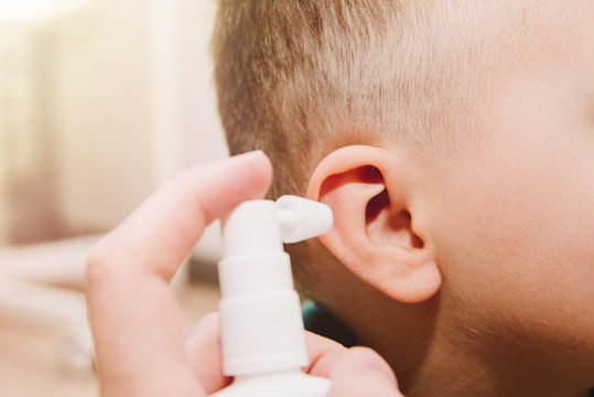 Using A Spray To Clean The Child's Ears. Medical And Health Concept, Colds. The Father Cleans The Child's Ears, Clogged By The Secretion Of The Ear, The Cork. Hearing And Earache.