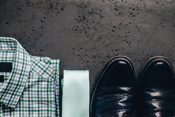 Top view of a business shirt, luxury shoes and a tie on a dark, stone table. The concept of fashion and sale of clothes for men, business and luxury shirts. The elegant look of men.