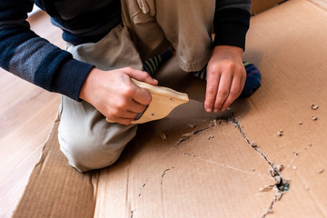 Child playing with a cardboard box and a saw to build.