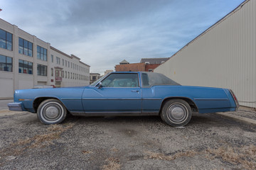 Long blue seventies style car parked in urban industrial area