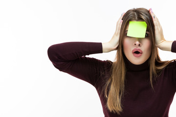 Portrait of Forgetful Surprised Caucasian Woman in Burgundy Turtleneck Sweater With Yellow Sticky Note on Her Forehead. Posing Against White Background.