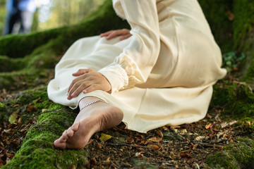 Mujer descalza con vestido blanco, sentada sobre la raíz de un árbol de haya