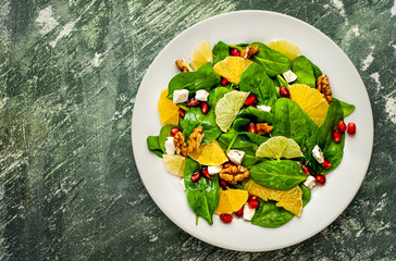 salad with spinach, orange, lemon, pomegranate, feto cheese, walnut on a white plate against the background of slate, stone or concrete