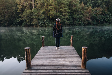 female Traveler sit on the Bamboo bridge beside the lake in the mist at morning sunrise at Pang Ung , Mae Hong Son province, Thailand