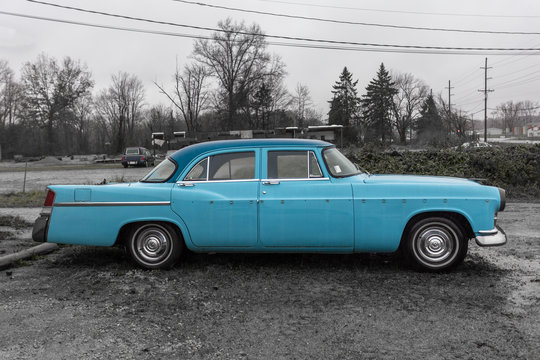 Classic fifties style blue car with shiny hubcaps retired in parking lot